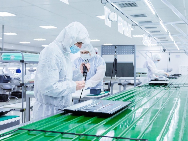 factory workers in white lab suits and face masks producing tv sets on a green assembly line with some modern equipment scaled